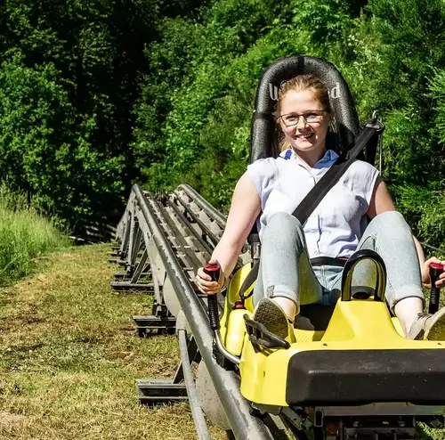 Eine Frau auf einem Alpine Coaster Schlitten lächelt am Standort der Sommerrodelbahn Gutach in die Kamera.