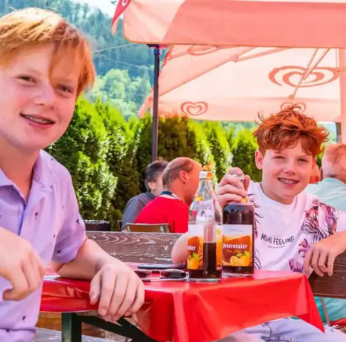 Zwei Jugendliche lächeln im Imbiss der Sommerrodelbahn Gutach in die Kamera, im Hintergrund eine bergige Landschaft.