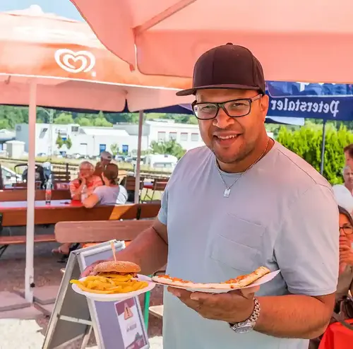 Ein Mann steht mit Essen und Trinken in der Hand im Biergarten der Sommerrodelbahn Gutach.