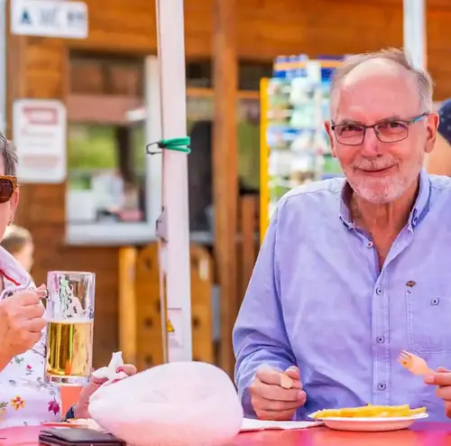 Ein älterer Herr und eine Frau sitzen an einem Tisch im Biergarten der Sommerrodelbahn Gutach, trinken Bier und essen Pommes.