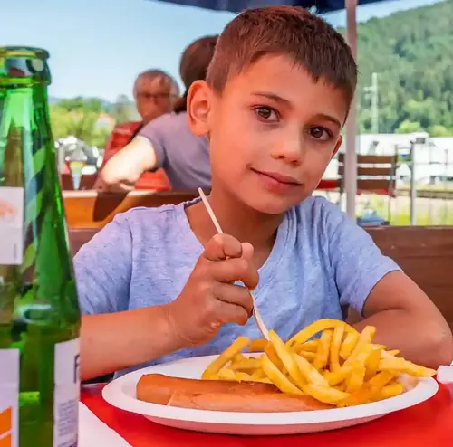 Ein Kind sitzt im im Imbissbereich der Sommerrodelbahn Gutach, im Hintergrund eine bergige Landschaft.
