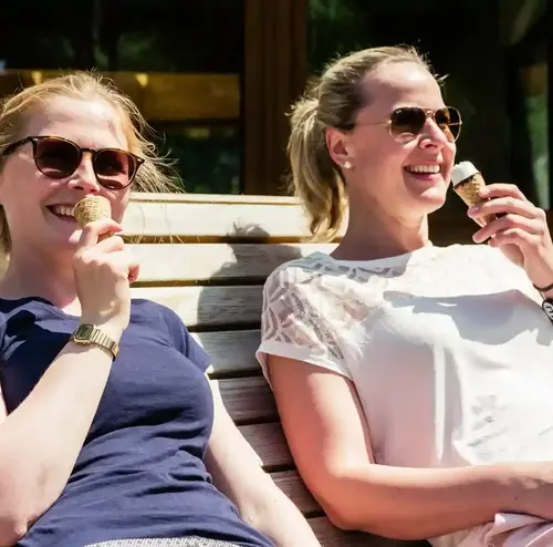 Zwei Frauen sitzen lächelnd auf einer Bank im Freizeitpark Sommerrodelbahn Gutach und essen Eis.